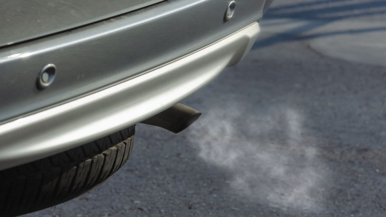 Sortie d'échappement d'une voiture argentée émettant de la fumée